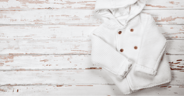 Soft white baby hoodie and clothing for infants on white wooden background.