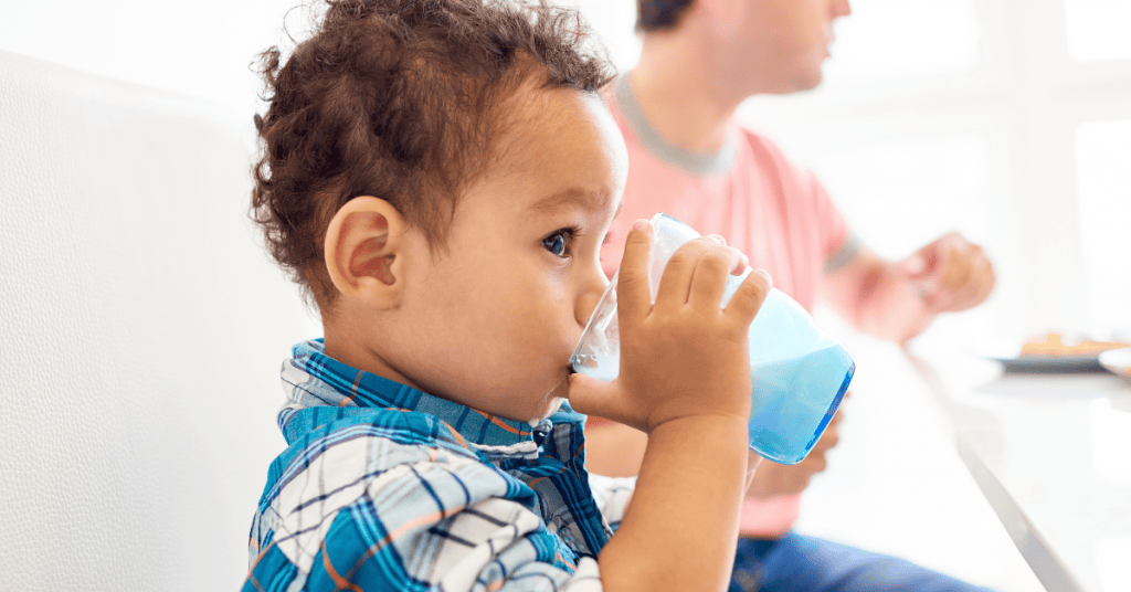 Cute toddler drinking blue juice, wearing plaid baby clothes, from a baby clothes and toys store.