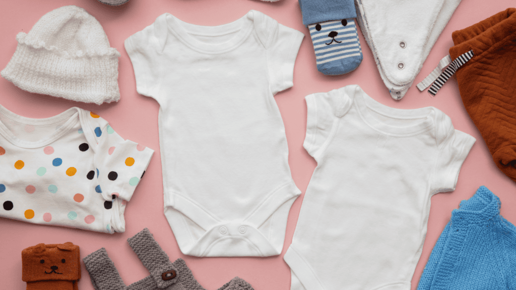 Soft baby clothes and toys with adorable accessories on pink background, perfect for newborns and infants.
