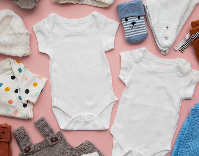 Soft baby clothes and toys with adorable accessories on pink background; perfect for newborns and infants.
