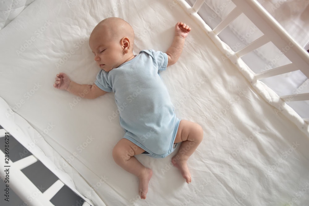 Top view wide angle sleeping newborn baby lies in a crib arms and legs outstretched