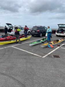 Alt tekst: Grupper forbereder kajakker på parkeringsplads til en dag ved vandet.