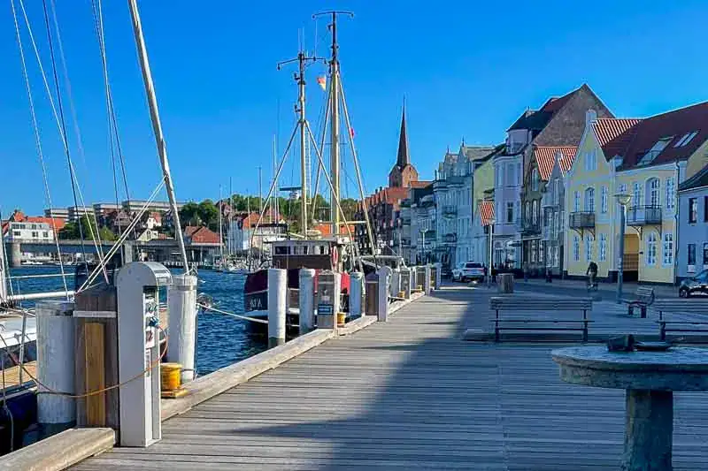Udsigt over havnen med træbrygge, både og farverige bygninger under en klar blå himmel