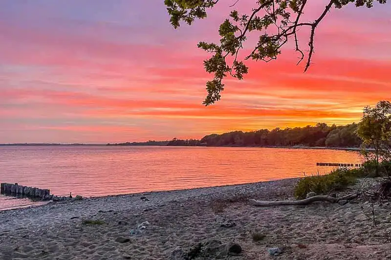 Solnedgang over strand og vand med farver i himlen og en rolig kystlinje.