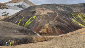 Vandrere på sti gennem mørke vulkanske bjerge med sne og grøn mos i Landmannalaugar