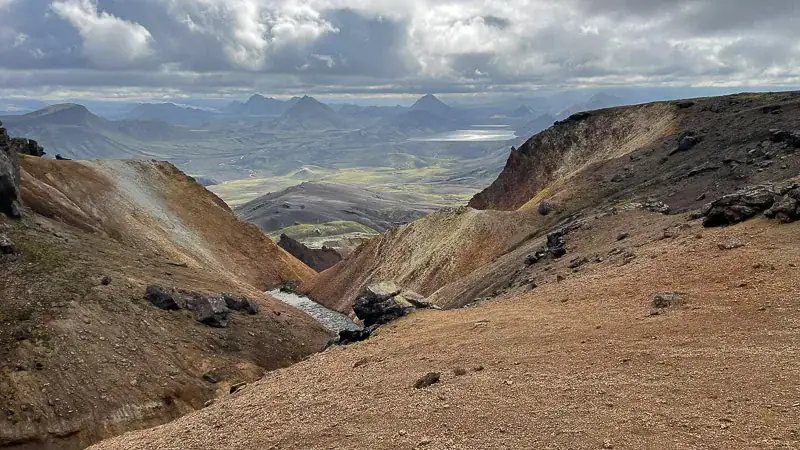 Farverigt vulkansk landskab med bjerge og dal under dramatisk skyet himmel