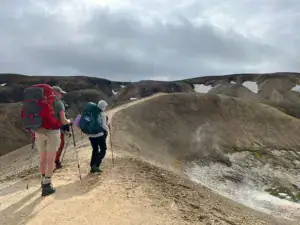 Tre vandre på stien Laugavegur der er pletter af is og sne i et bakket landskab