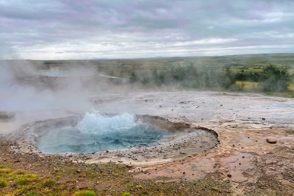 Naturdamp af varm kilde med boblende vand og damp, omgivet af islandske landskaber, perfekt til natur- og rejseoplevelser.