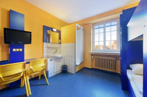 Economy Zimmer mit einem Etagenbett, Schreibtisch, zwei Stühlen, TV, Fenster, Waschbecken und eigener Dusche.