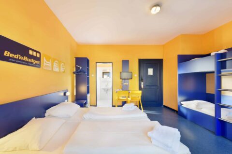 Comfort-Zimmer mit zwei Einzelbetten und zwei Etagenbetten für 6 Personen, Schreibtisch, zwei Stühle, Schrank und eigenem Badezimmer.