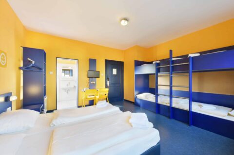 Comfort-Zimmer mit zwei Einzelbetten und zwei Etagenbetten für 6 Personen, Schreibtisch, zwei Stühle, Schrank und eigenem Badezimmer.