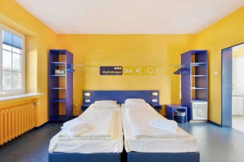 Comfort-Zimmer mit zwei Einzelbetten, zwei offenen Schränken, Safe, Kühlschrank und Verbindungstür rechts.