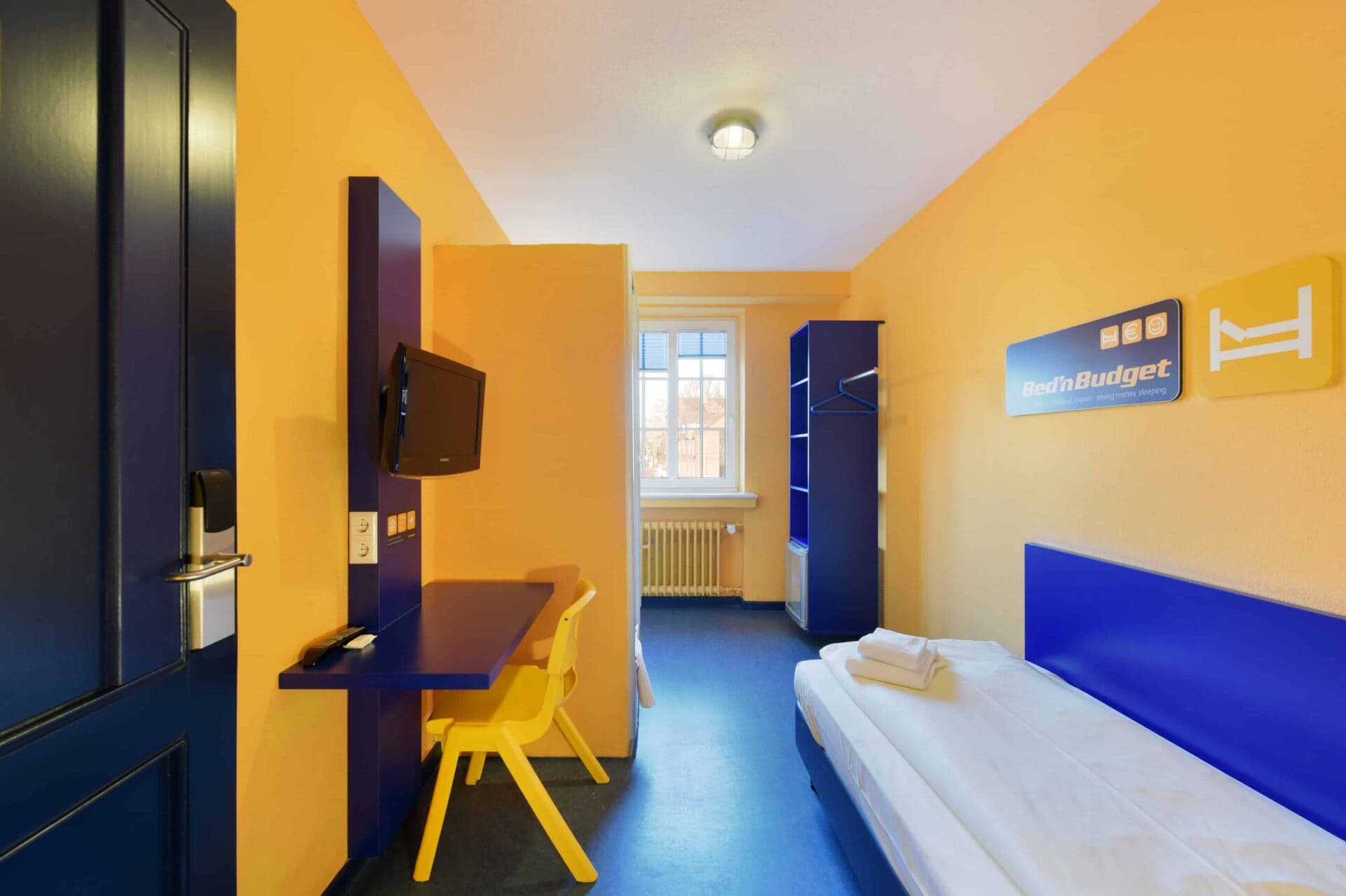 Economy-Zimmer mit einem Einzelbett, einem Schreibtisch, einem Stuhl, TV, Fenster und Schrank.