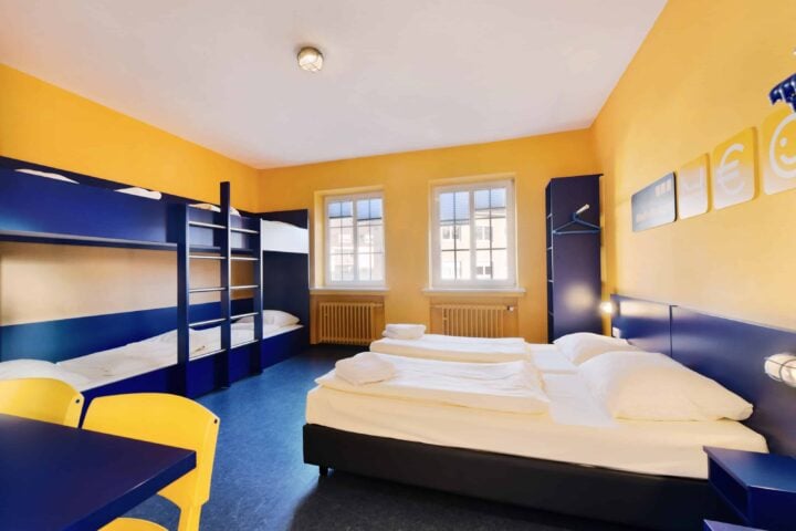Zimmer mit zwei Etagenbetten und zwei Einzelbetten für 6 Personen, einem Schrank, zwei Stühlen und Fenster.