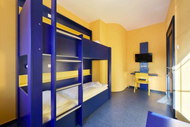 Zimmer mit einem Etagenbett für 2 Personen, Schreibtisch, Stuhl und TV.