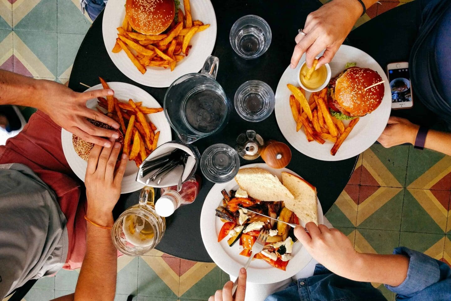 Four people eating together, top-down view of a table with burgers, fries, and drinks