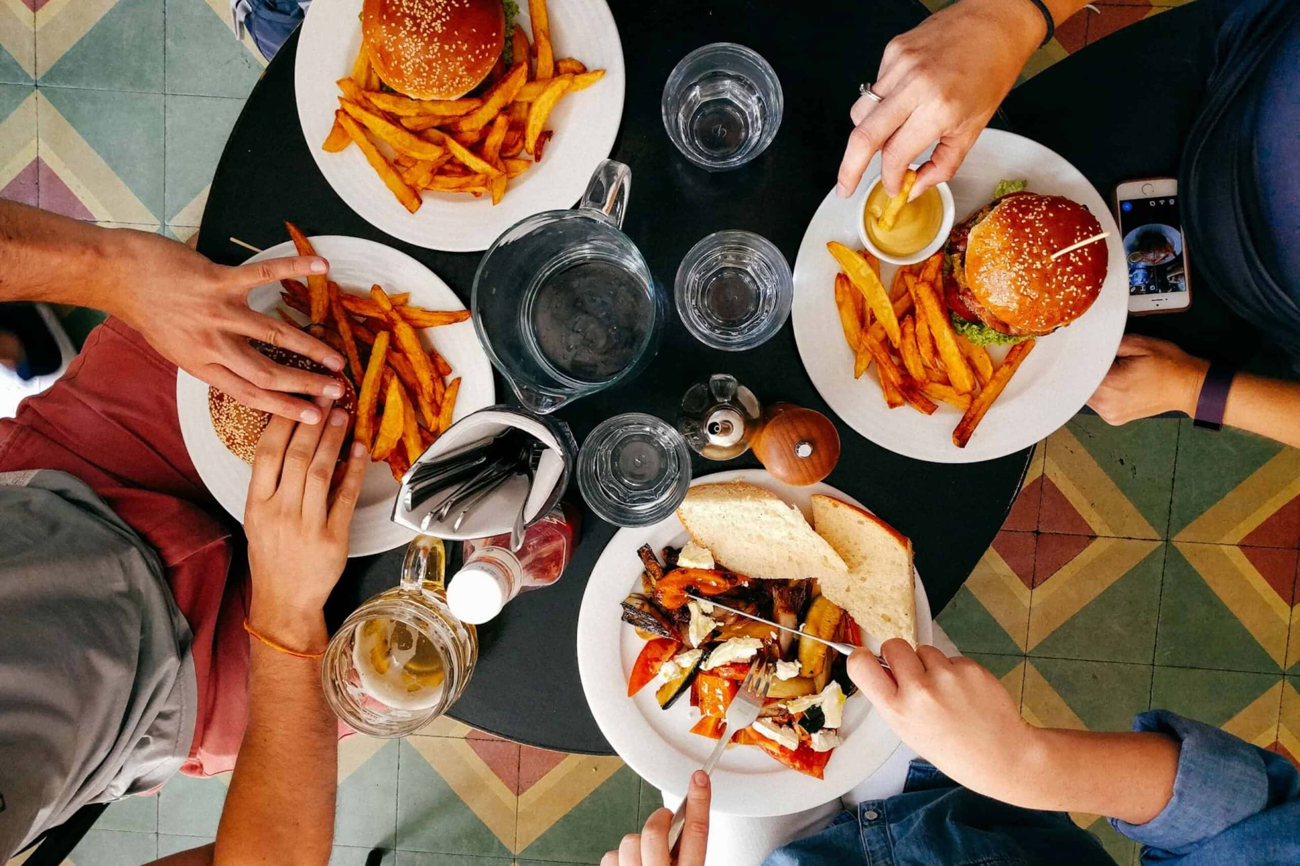 Vier Personen beim gemeinsamen Essen, Tisch mit Burgern, Pommes und Getränken von oben