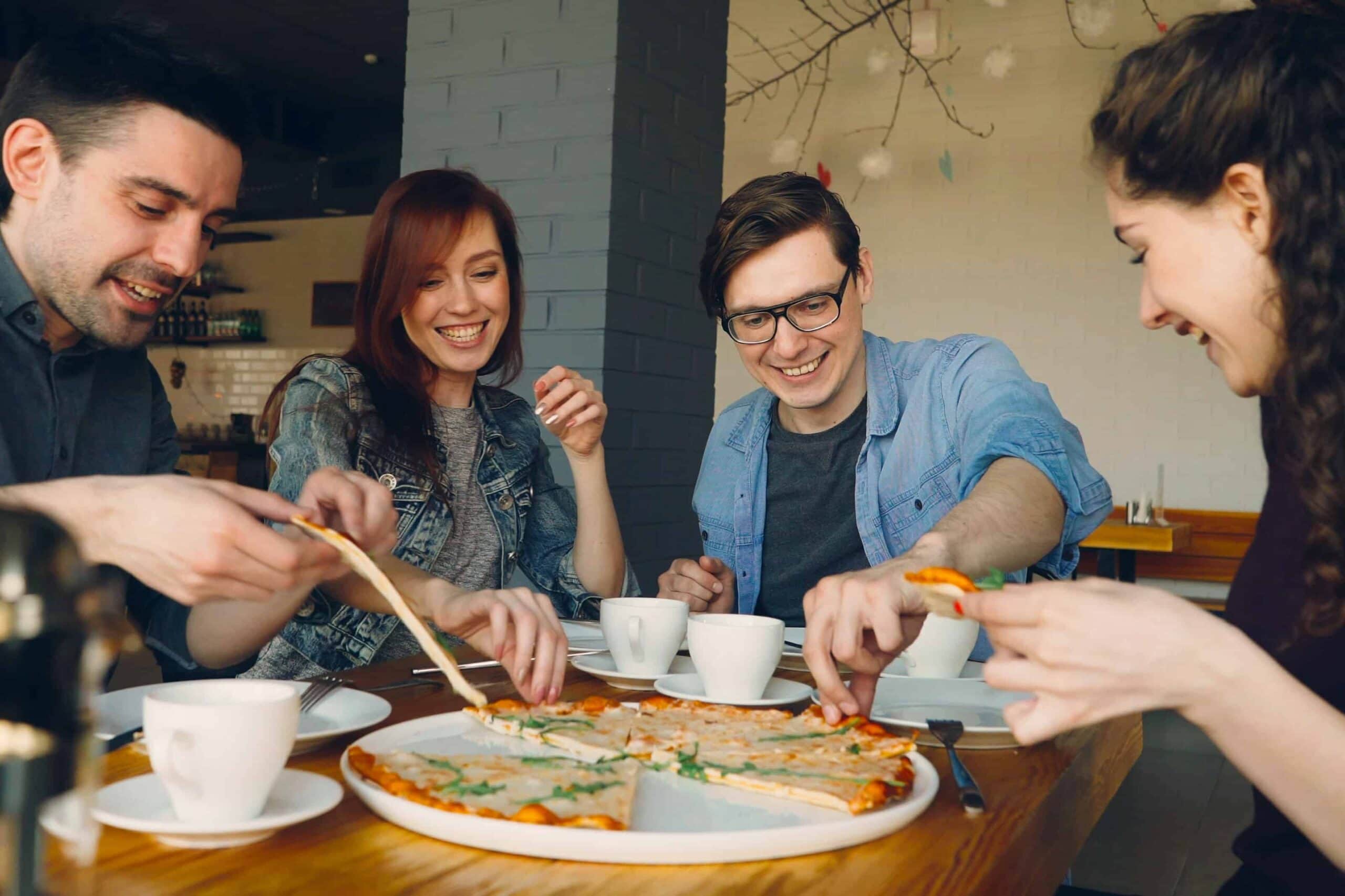 Four smiling people eating pizza.