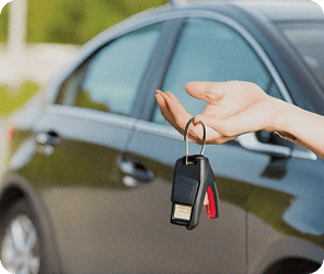Keyless car key fob being held next to a black sedan at Bee Clean car wash facility.
