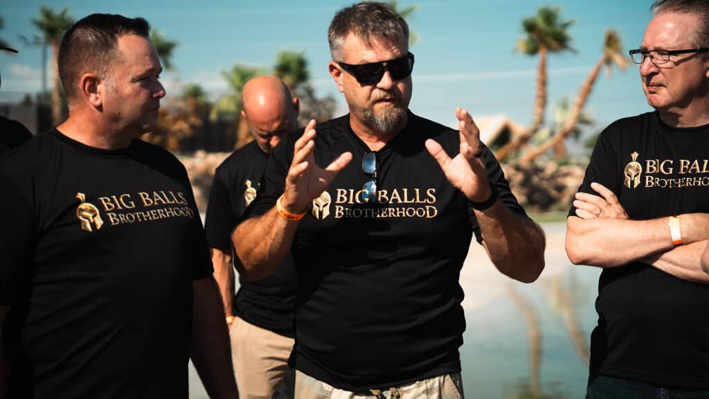 Bold men in black "Big Balls Brotherhood" T-shirts engaging in outdoor conversation at the event.