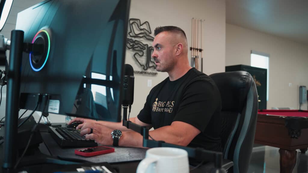 Male gamer at a computer wearing a Big Balls Brotherhood T-shirt, focused on gaming in a modern gaming setup.