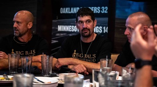 Focused men wearing Big Balls Brotherhood T-shirts sitting at a dining table during a gathering or event, emphasizing camaraderie and brotherhood.