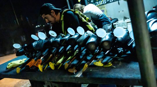 Black and yellow golf clubs lined up on a table at Big Balls Brotherhood, with a man inspecting equipment at night, emphasizing camaraderie and sportsmanship.
