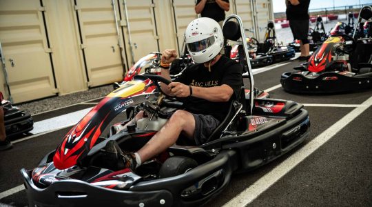 High-speed go-kart racing at Big Balls Brotherhood track, featuring racers with helmets and racing suits, showcasing adrenaline-pumping motorsport fun and competitive karting experiences.