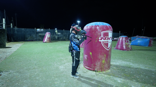 Dramatic night-time paintball game at Big Balls Brotherhood field with players wearing protective gear and tactical clothing. Fast-paced action and strategic gameplay on illuminated paintball arena.