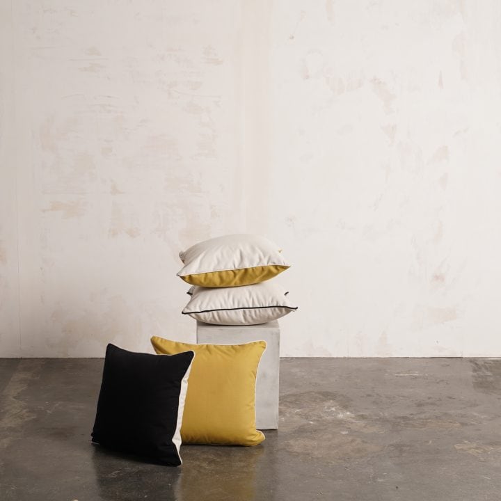 Cojines Fara en negro, amarillo y blanco apilados sobre un pedestal