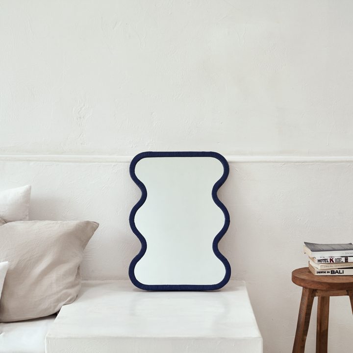 Espejo de ratán azul Lima junto a un taburete de madera