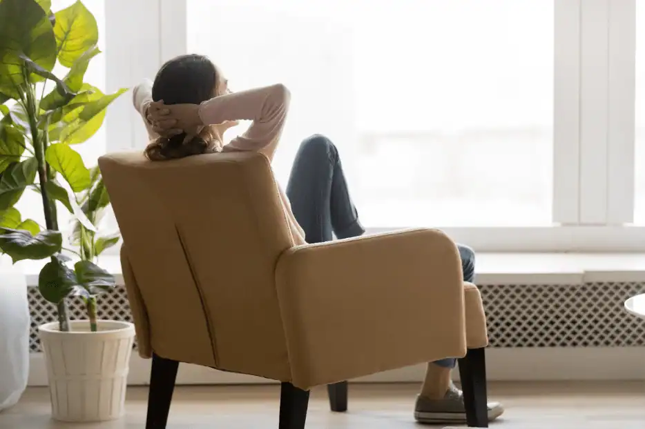 A Bonfe team member relaxes in a beige armchair with legs crossed and hands behind their head, enjoying the view through a large window. A potted plant adds a touch of greenery to the left side in this welcoming Bonfe Insider September 2020 setting.