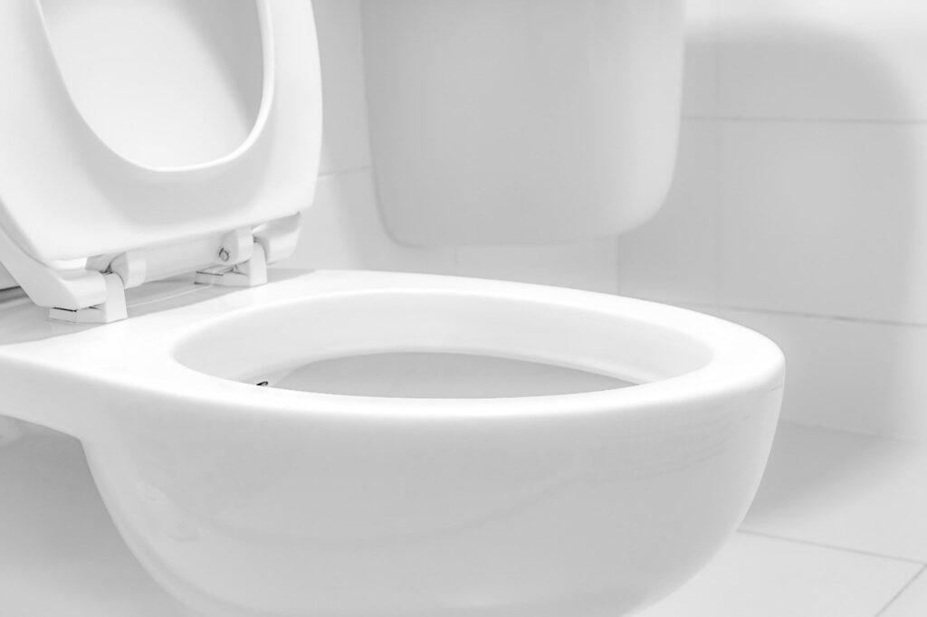A clean, white wall-mounted toilet with the lid open is shown in a bright, white-tiled bathroom, highlighting Bonfe’s quality bathroom services as featured in the July 2021 Bonfe Insider.