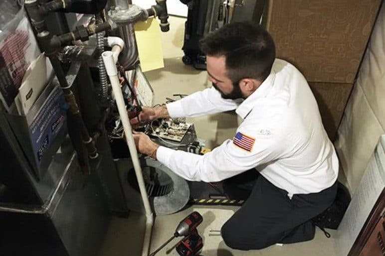A Bonfe technician in uniform kneels in a utility room, carefully repairing or inspecting a furnace with professional tools arranged nearby, providing expert service as part of the Bonfe team.