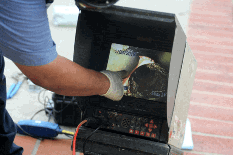A Bonfe technician, wearing protective gloves, uses a camera inspection device to examine the inside of a pipe. The monitor screen clearly displays the pipe’s interior as part of Bonfe’s expert services, featured in the November 2021 edition of the Bonfe Insider.