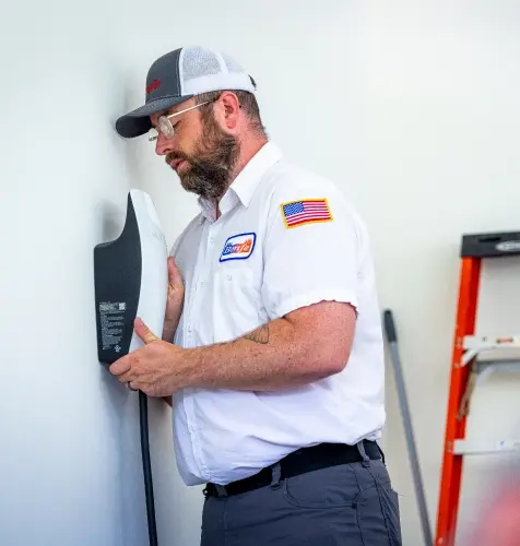 A Bonfe technician in uniform professionally installs an electrical device on a white wall, with a ladder and broom nearby as part of Bonfe’s reliable service setup.