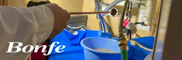 A Bonfe technician works on plumbing beneath a sink, using professional tools alongside visible hoses and a blue bowl. The text “Bonfe Insider May 2025” is displayed in the lower left corner.