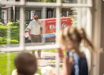 A Bonfe delivery team member stands outside next to a red service truck, while two excited young customers watch from inside through a window, eagerly awaiting their Membership Plan package.