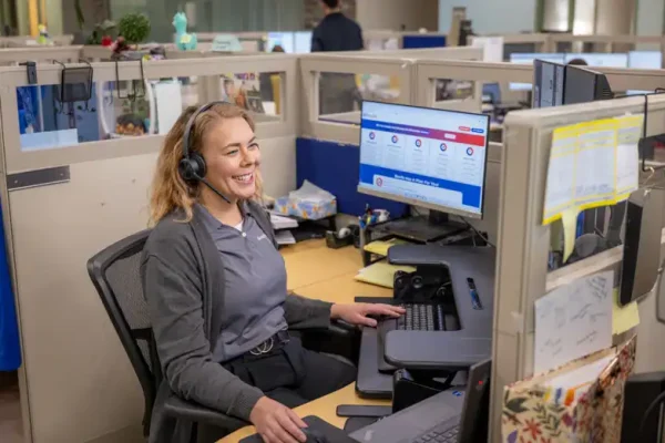 A Bonfe team member wearing a headset sits at her desk in a modern office cubicle, warmly smiling at her computer monitor as she assists customers with exceptional service.
