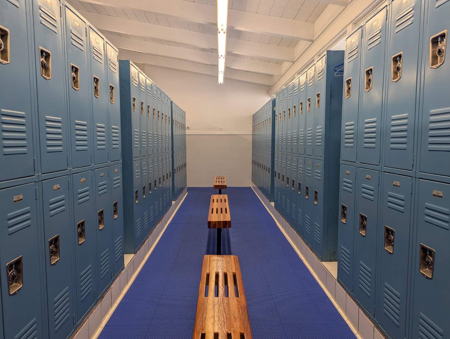 Locker room at Bay-O-Vista Swim & Tennis Club with blue lockers and wooden benches, ideal for swimmers and tennis players.