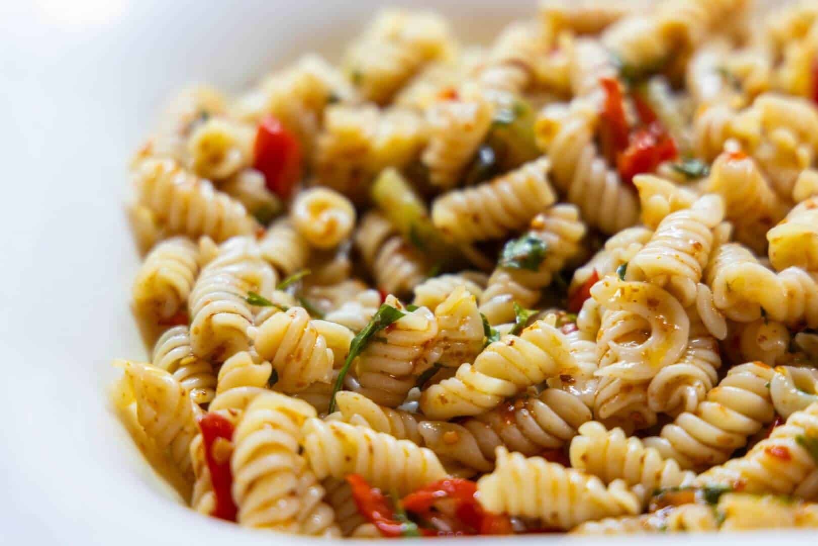 Healthy whole wheat pasta salad with cherry tomatoes, spinach, and herbs, served on a white plate. Perfect for summer meals or outdoor gatherings, showcasing fresh ingredients and vibrant flavors.