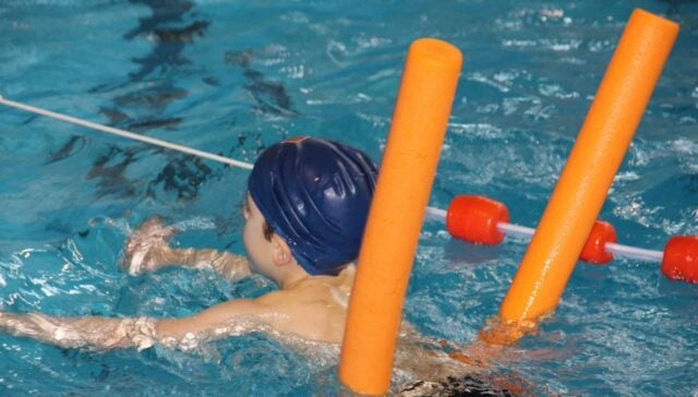 Child taking swim lessons with instructor in the Bay-O-Vista pool - learning water safety skills in San Leandro