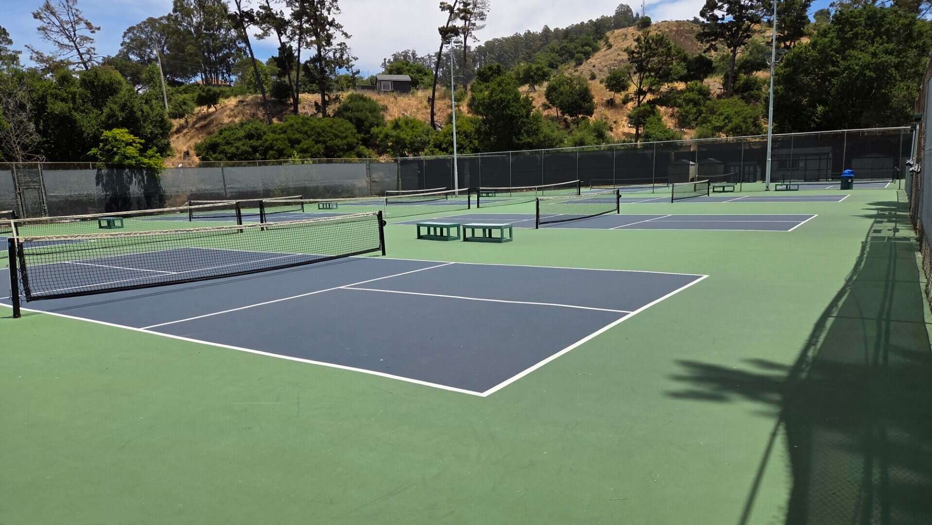 Bright blue and green tennis courts at Bay-O-Vista Swim & Tennis Club with surrounding trees and scenic hills in the background.