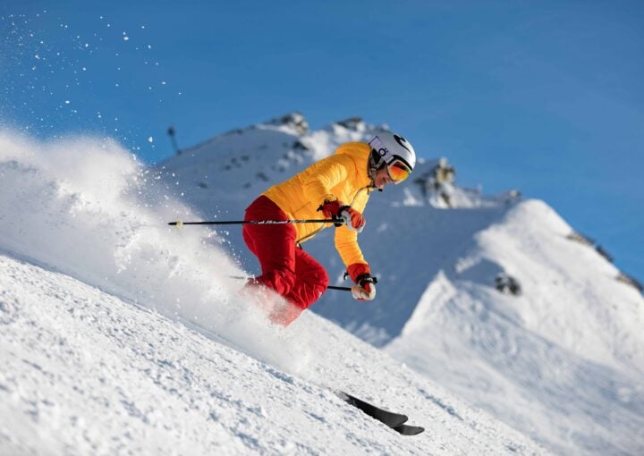 Dynamic skier in bright yellow jacket and red pants enjoying winter sports on snowy mountain slope beneath clear blue sky at Bay-O-Vista Swim & Tennis Club.