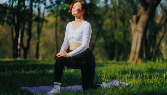 Woman practicing yoga outdoors in a park during summer, promoting fitness and wellness.