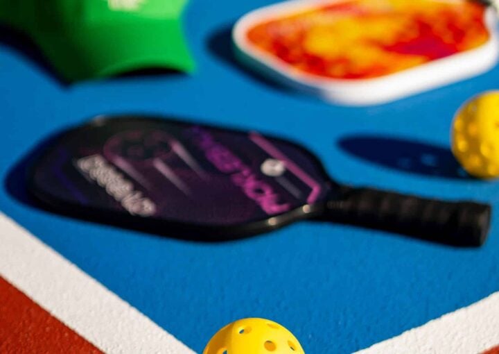 Sports equipment at Bay-O-Vista Swim & Tennis Club including tennis rackets, balls, and a paddle on a blue court surface.