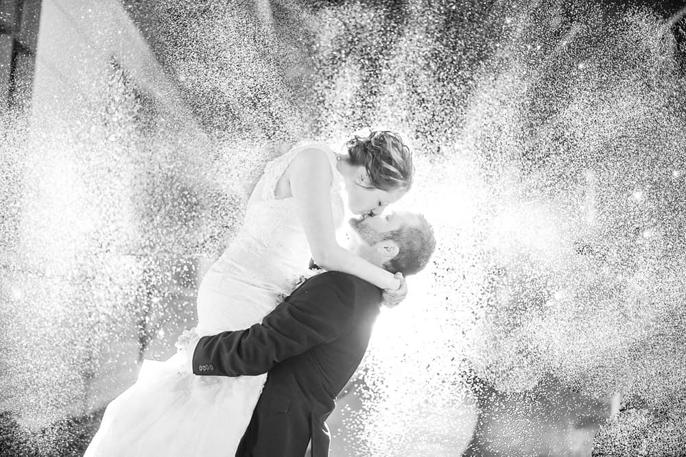A La Crosse WI wedding photographer captures the bride and groom's kiss in front of a spray of water.