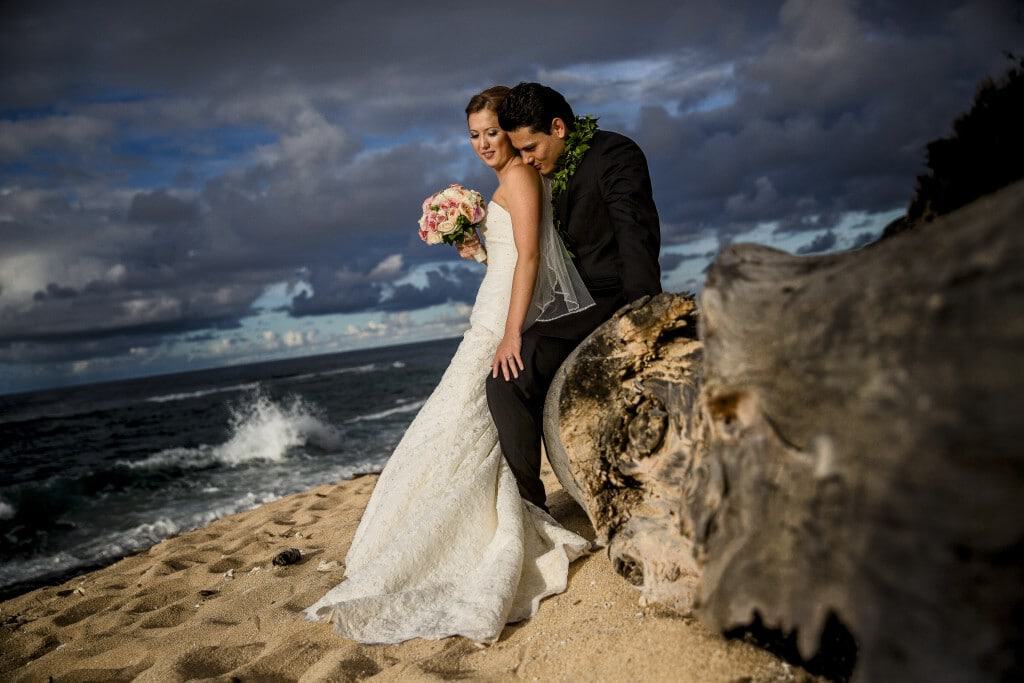 hawaii wedding beach bride and groom A bride and groom posing on a log on the beach.