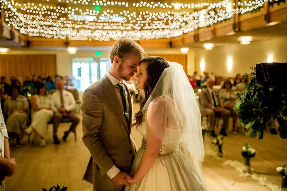 A bride and groom share their first kiss at a Silverthorne, CO wedding under string lights.