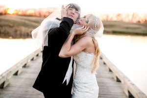 A magazine-worthy wedding photo featuring a bride and groom embracing on a picturesque dock at sunset.